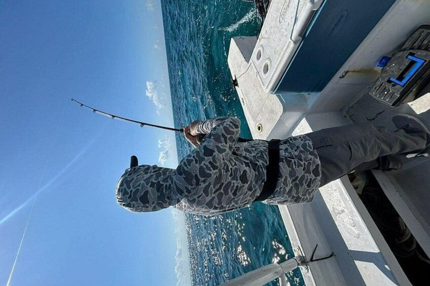 A person fishing on a boat with a clear view of the ocean and distant land. 3