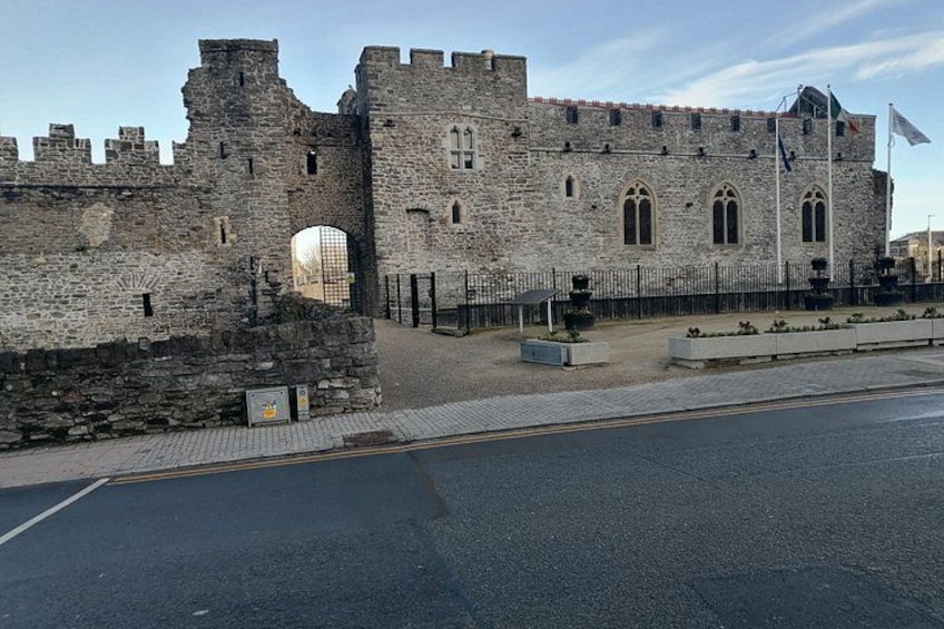 Un château de pierre historique, avec une grande porte, un mât et une route pavée au premier plan. 1