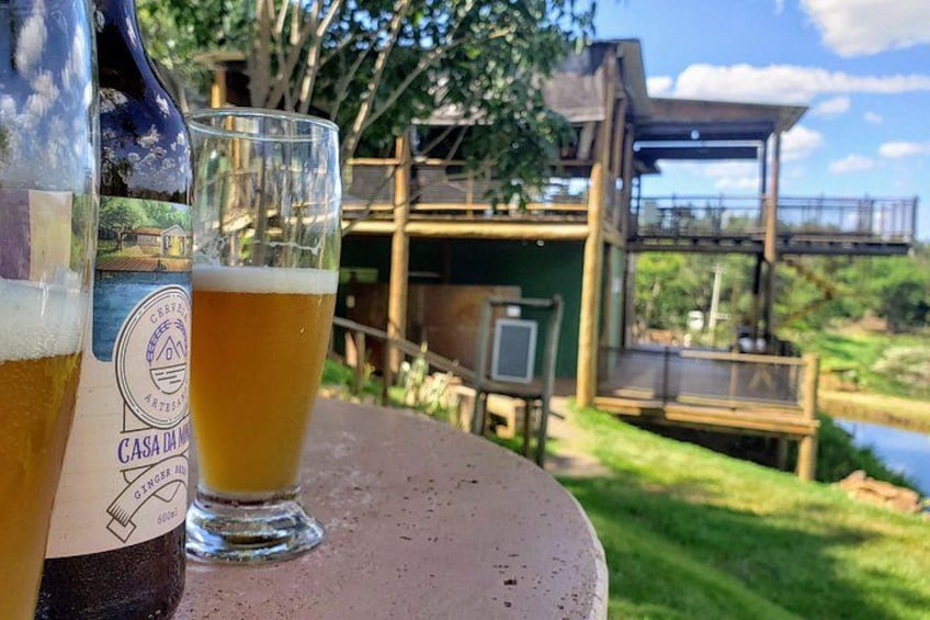 A beer bottle and glass on a table with a rustic wooden structure and a river in the background. 4