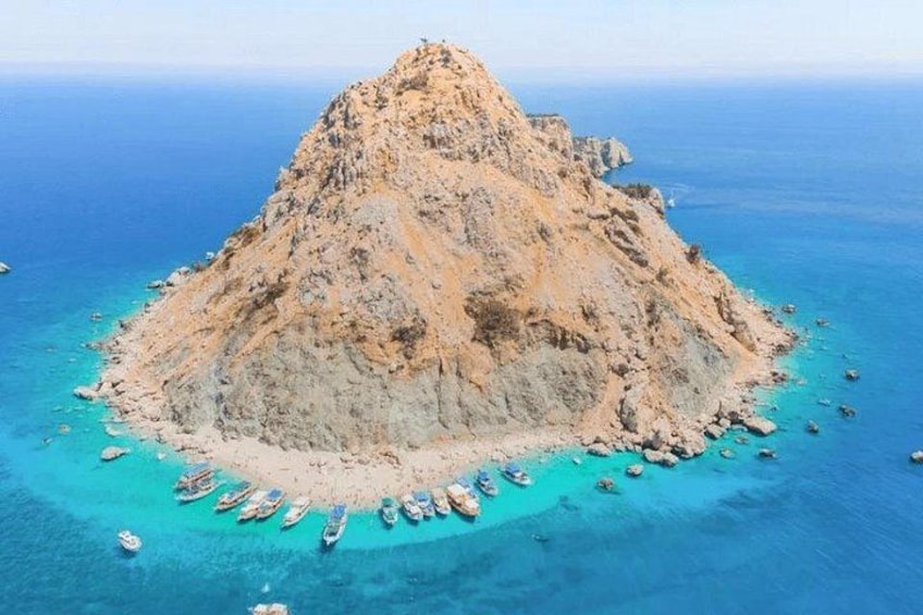 Een rotsachtig eiland omgeven door turquoise water, met enkele boten afgemeerd bij de kust. 4