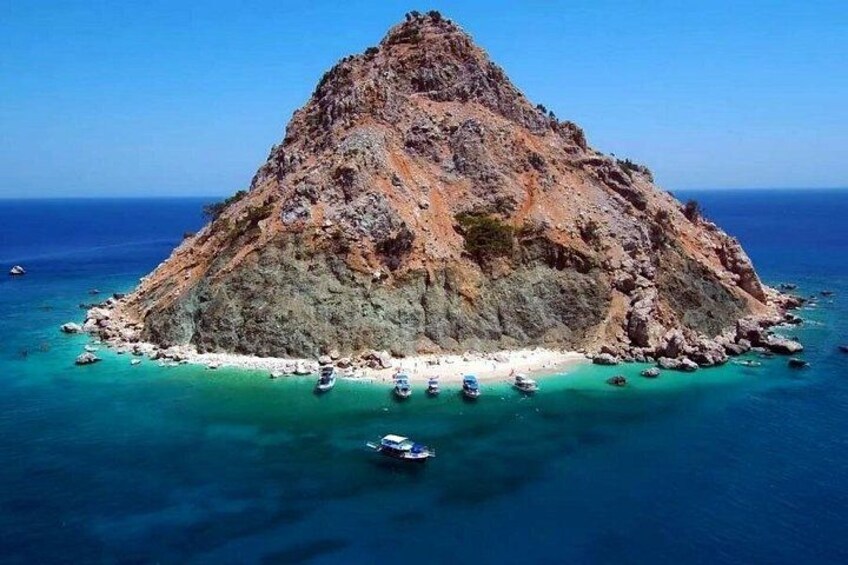 Een rotsachtig eiland met helder turquoise water, boten die aan de kust liggen ankeren en een strakblauwe lucht. 3