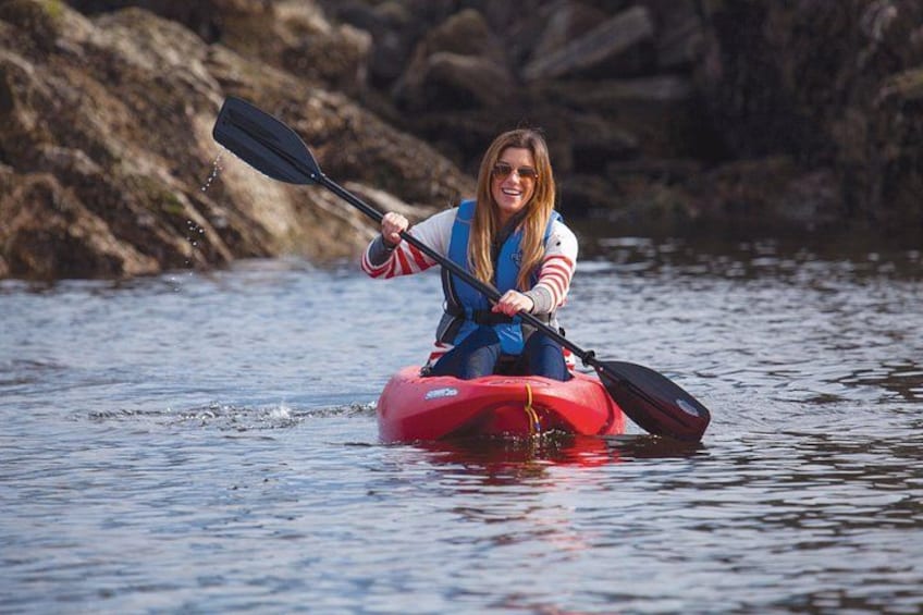 A person kayaking on a calm body of water with rocks in the background. 4
