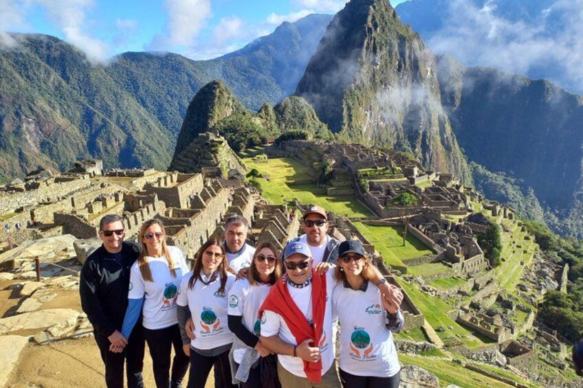 Un gruppo di persone in piedi di fronte a Machu Picchu, con le famose rovine inca e le montagne circostanti sullo sfondo. 1