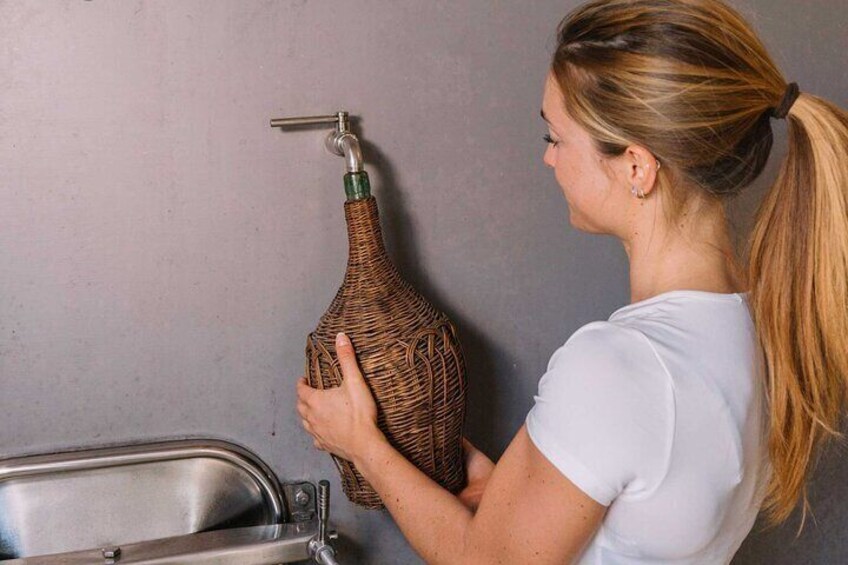 A person holding a large, woven bottle near a sink. 5