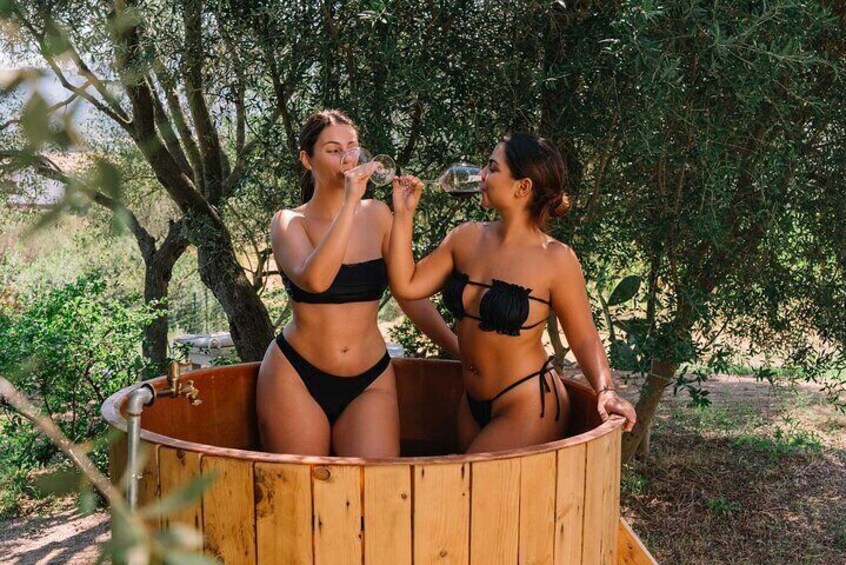 Two people in a wooden hot tub outdoors surrounded by trees. 4