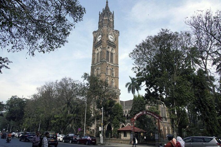 A historic clock tower, a busy street, and surrounding trees. 2