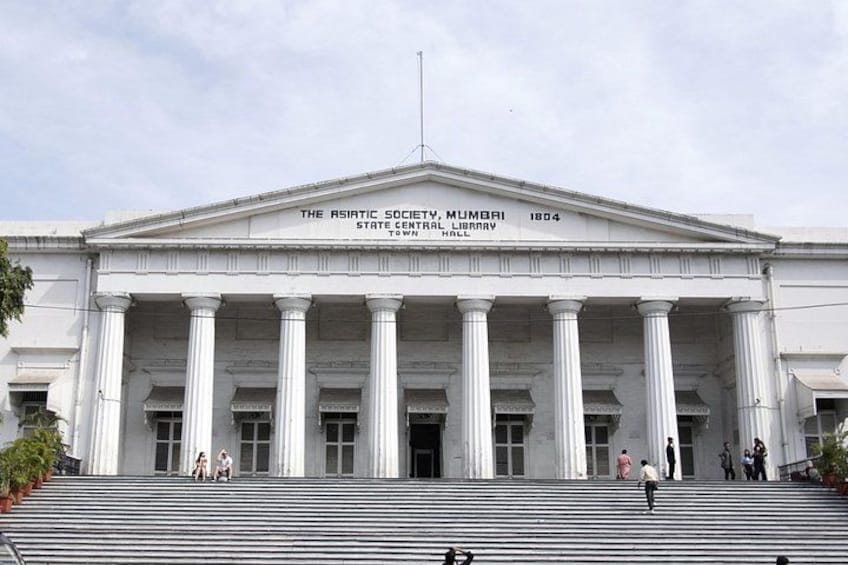 A grand building with a classical architectural style, featuring a large central entrance flanked by columns, and a sign indicating it is the Asiatic Society Library. 1