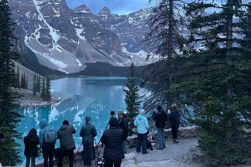 Un grupo de personas sobre un sendero mirando un lago con montañas al fondo. 3