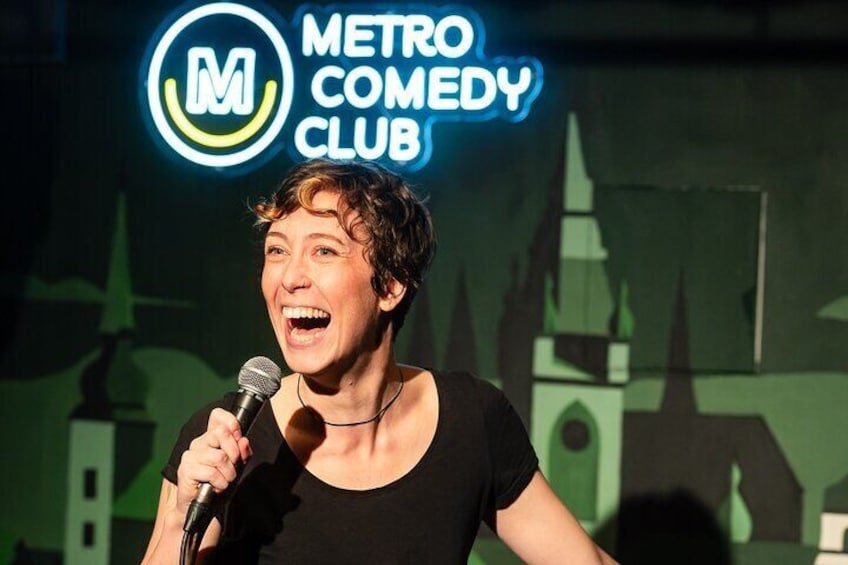 A person holding a microphone in front of a sign that reads "METRO COMEDY CLUB". 1