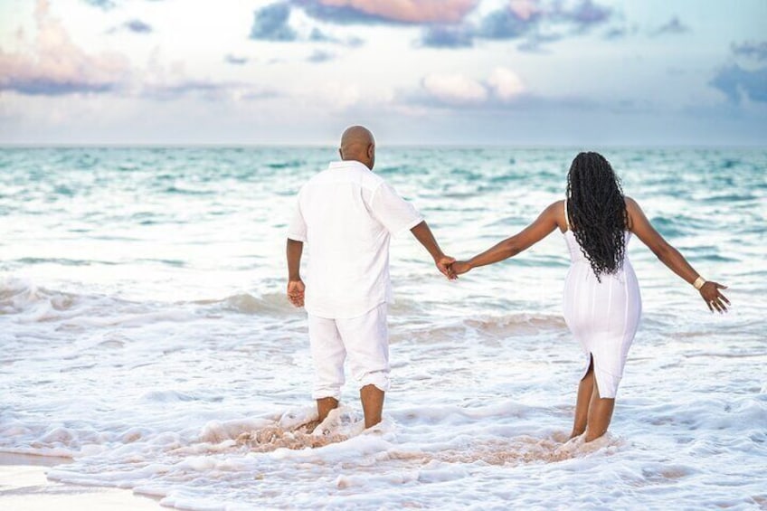 A couple holding hands walking on a beach with the ocean in the background. 2