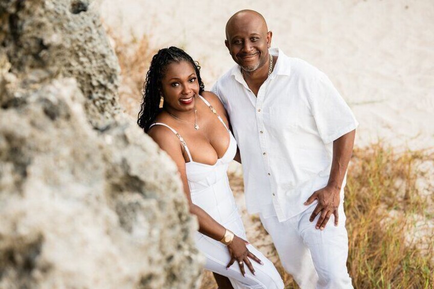 A couple standing on a beach with a large rock formation in the foreground. 3