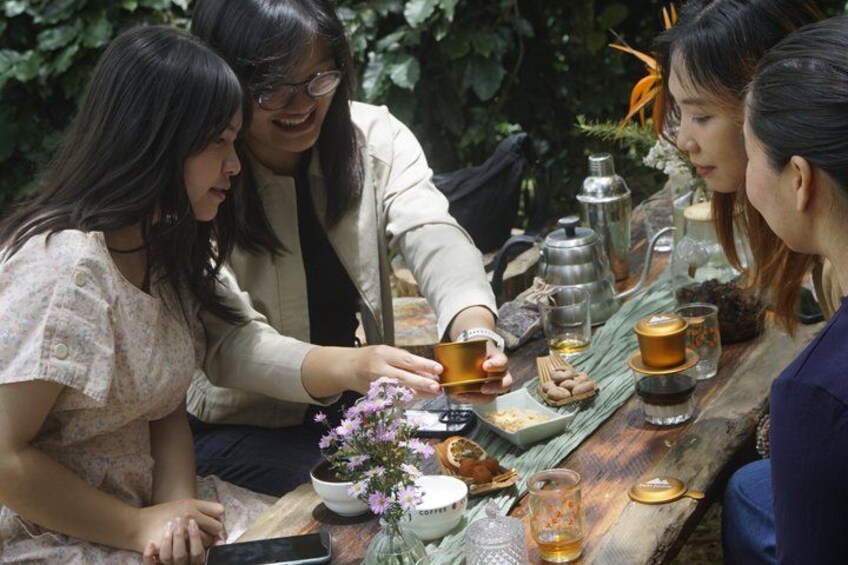 A group of people sitting at a wooden table outdoors, engaged in conversation. 4