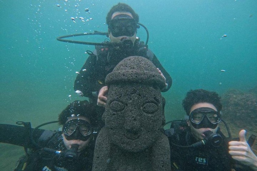 Drie duikers onderwater, met een groot, ge текстуerd object in het midden. 1