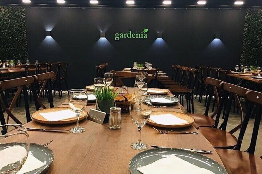 A restaurant interior with tables set for dining, a 'gardenia' sign on the wall, and wooden chairs. 4