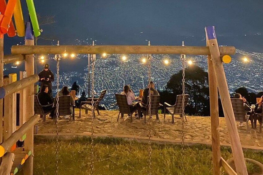 A swing set with people sitting and swinging on a beach at night. 3