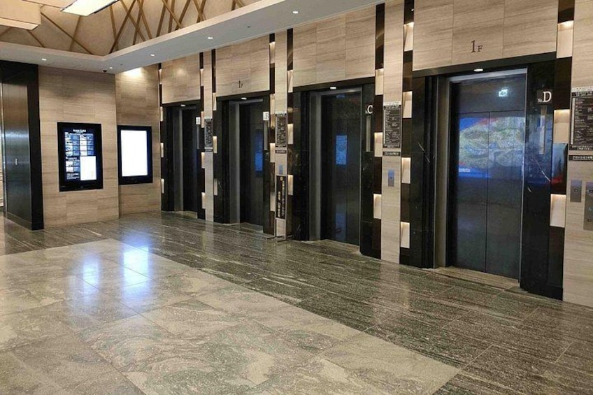 A modern elevator lobby with multiple elevators, polished marble flooring, and digital displays on the walls. 3