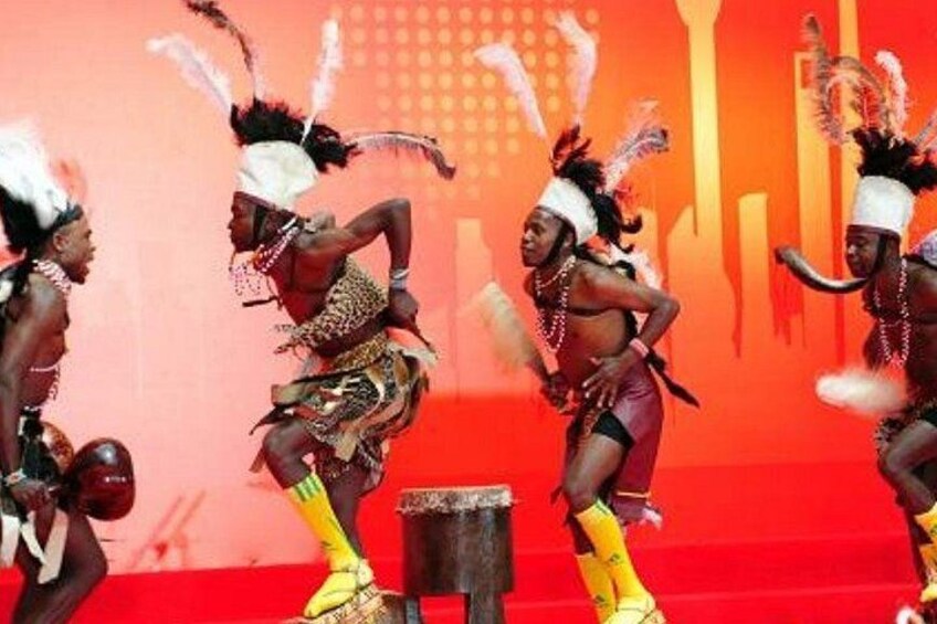 Un grupo de bailarines con trajes tradicionales se presenta en un escenario con fondo rojo. 2
