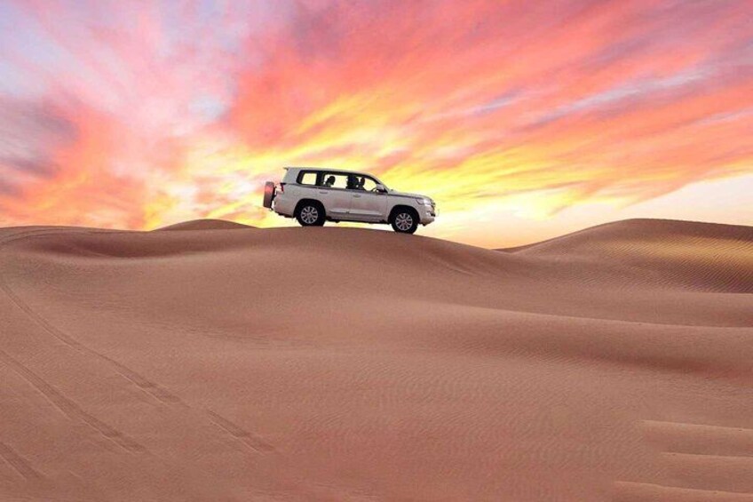 A white SUV on a sand dune with a sunset in the background. 2