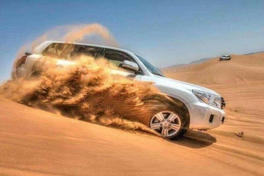 A white SUV driving through a desert with sand being kicked up by its tires. 4