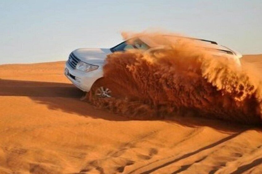 A white SUV driving through a desert with sand being kicked up by its tires. 3
