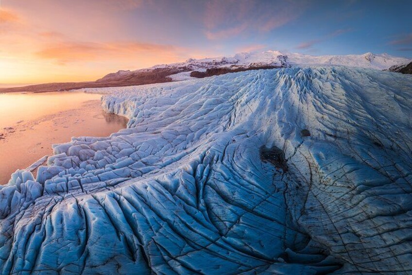 A glacier with a smooth, icy surface and a calm body of water in the foreground. 3