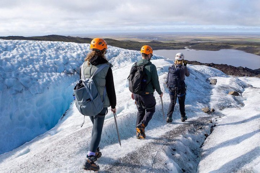 Three people hiking on a snowy mountain with a glacier and a lake in the background. 3