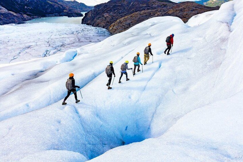 A group of hikers ascending a snow-covered glacier with a glacier lake in the background. 1