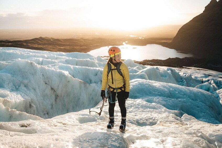 A person wearing an orange helmet and yellow jacket smiles while pausing during a glacier hike. 4