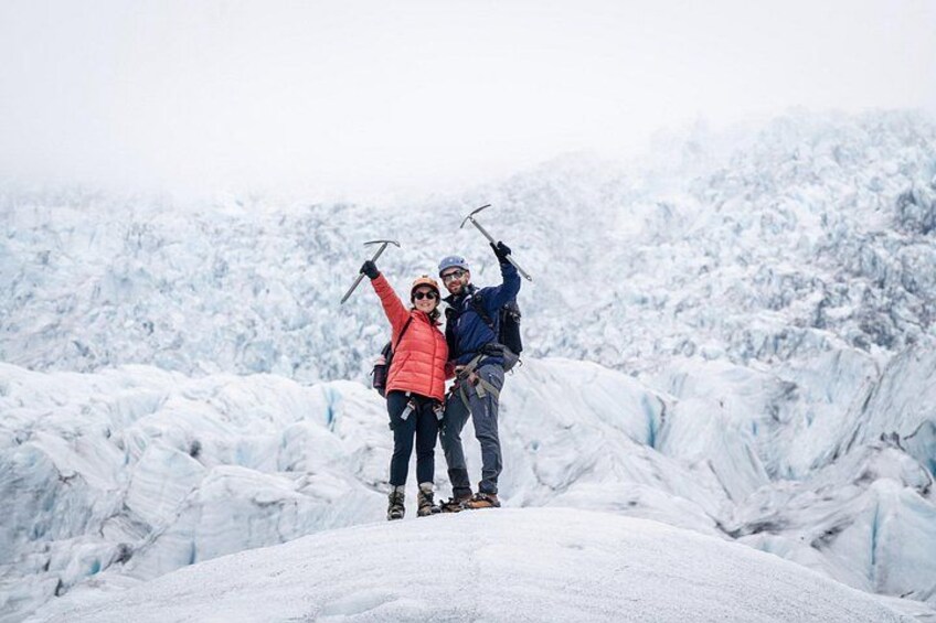 Two people standing on a snow-covered peak with ski poles, surrounded by a snowy mountainous landscape. 2