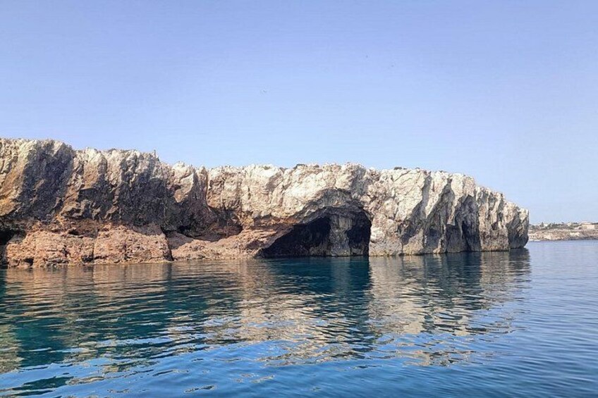 A coastal cliff with a cave entrance, calm sea, and clear sky. 4
