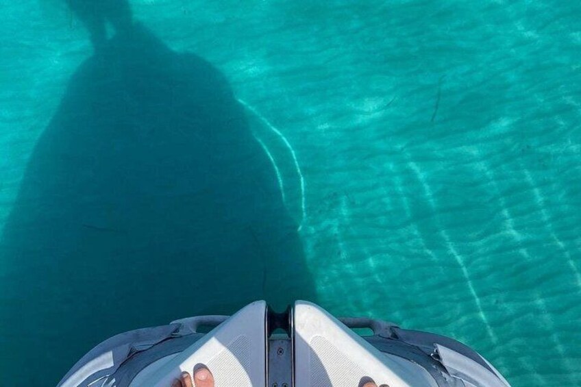 A boat on a turquoise water surface with a shadow of a person and a part of a boat visible. 3