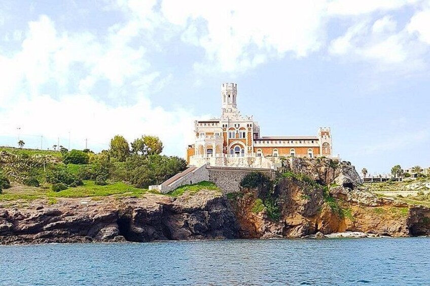 A historic building with a tower, situated on a rocky coastline with a body of water in the foreground. 5