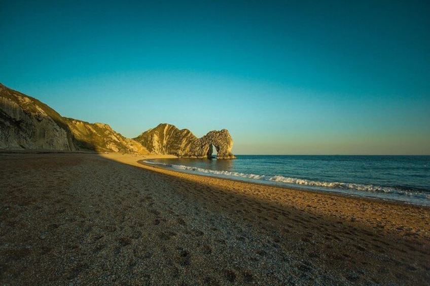 A beach with a rocky outcrop in the distance, a clear sky, and calm sea. 4