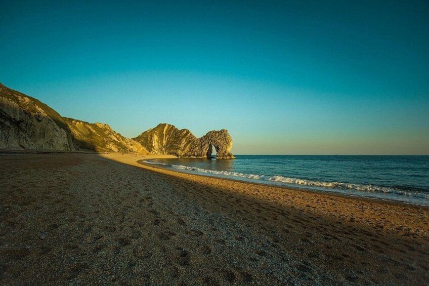 A beach with a rocky outcrop in the distance and a clear sky. 4