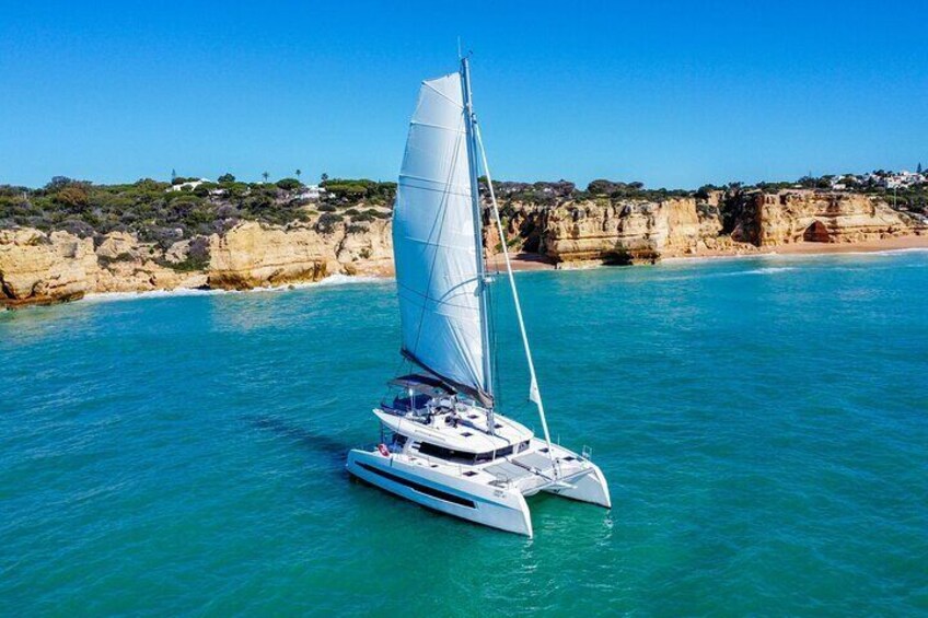 Un trimarán blanco navega sobre aguas turquesas cerca de una costa rocosa con acantilados y vegetación escasa. 3