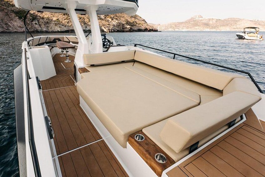 A boat deck with a cushioned seating area, wooden flooring, and a steering wheel. 2