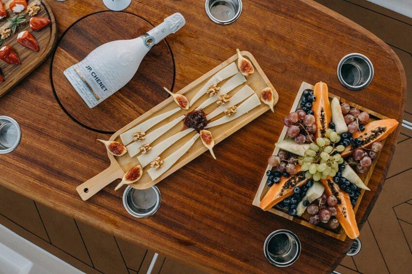 A wooden table with a bottle of wine, a fruit platter, and several glasses. 4
