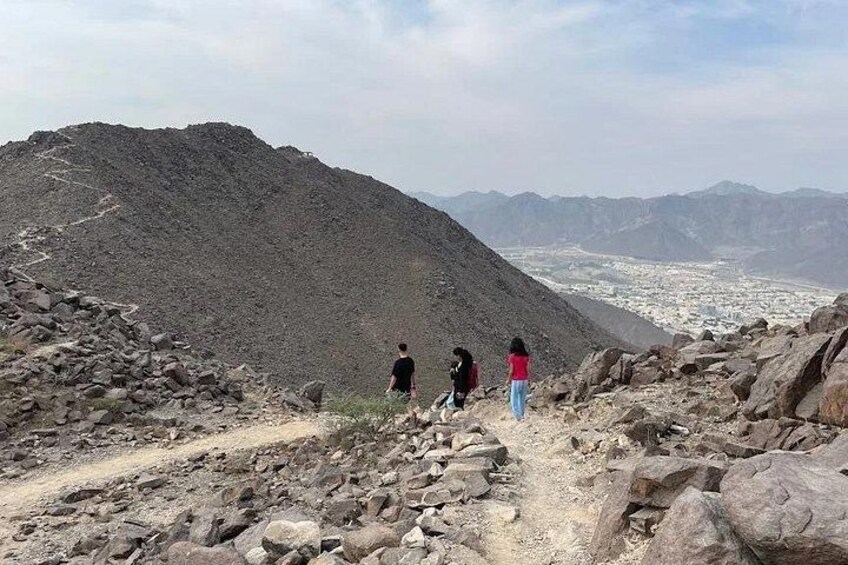 A rocky mountain path with hikers and a distant city view. 4