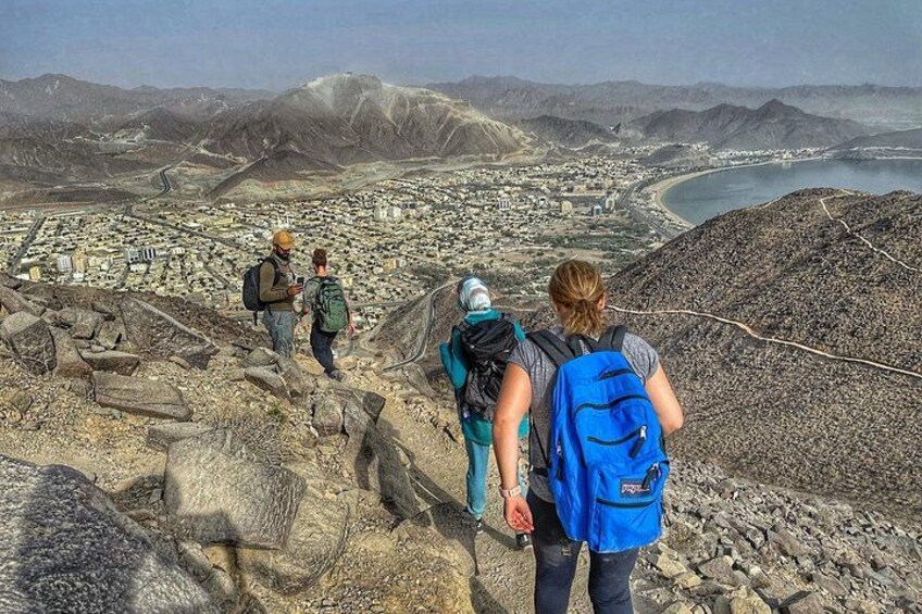 Hikers on a rocky trail with a city and coastline in the background. 1