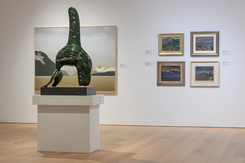 A sculpture on a pedestal, framed paintings on the wall, and a wooden floor. 2