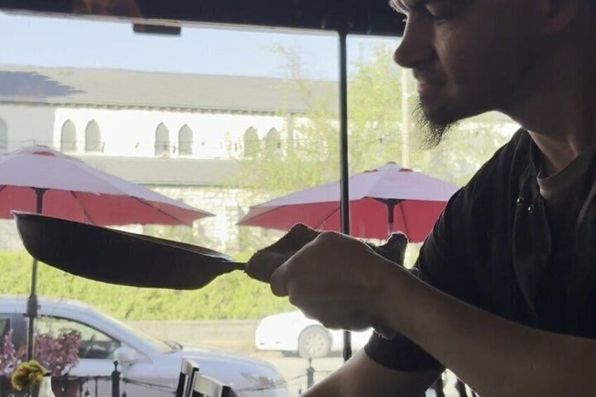 A person cooking outdoors with red umbrellas in the background. 1