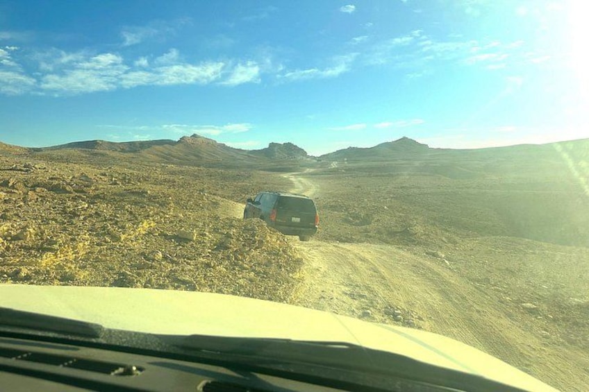A vehicle on a dirt road in a desert landscape with distant mountains. 4