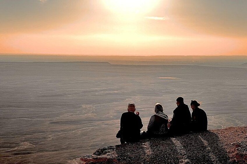 A group of people sitting on a rocky outcrop overlooking a vast salt flat at sunset. 5