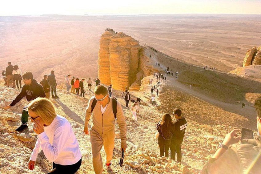 A group of people hiking on a rocky trail with a large rock formation in the background. 1