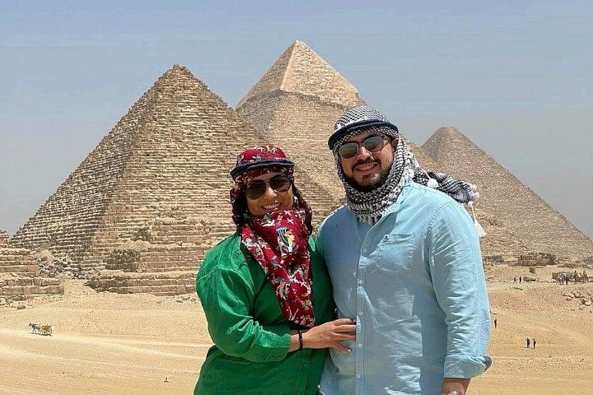 Two people standing in front of the pyramids with a desert landscape in the background. 5