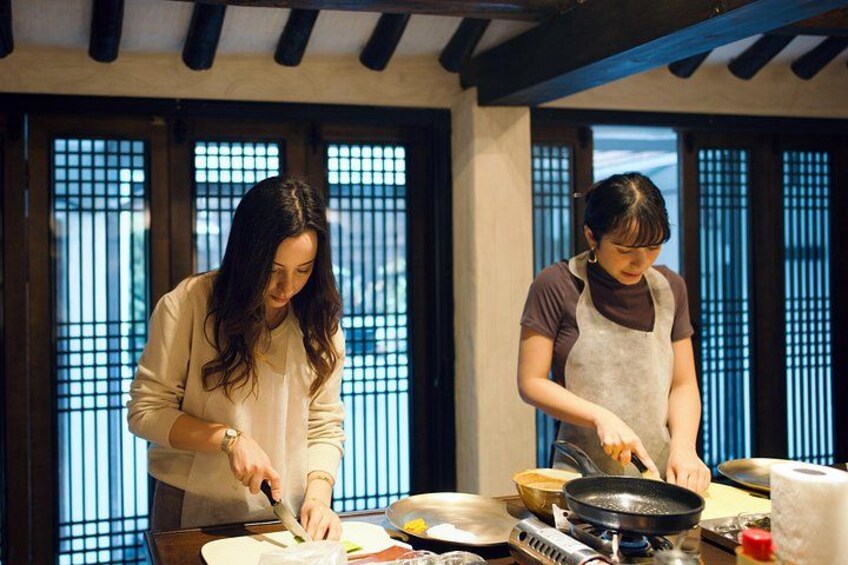 Two people cooking in a traditional kitchen with wooden beams and shoji screens. 1