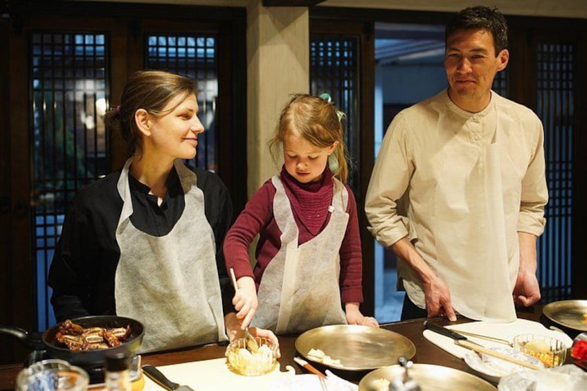 A family cooking together in a traditional kitchen with wooden cabinets and a stove. 3