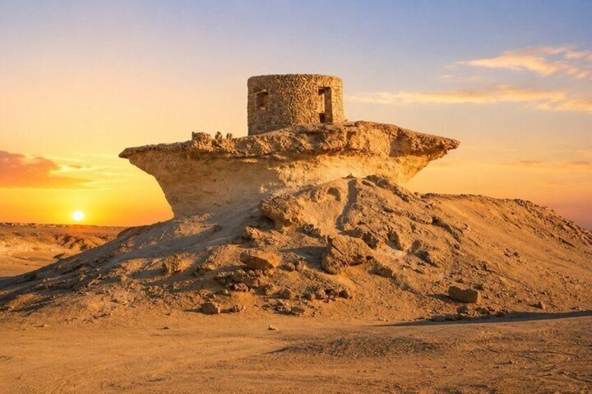 Paesaggio desertico con una formazione rocciosa imponente e una piccola struttura simile a una torre. 1