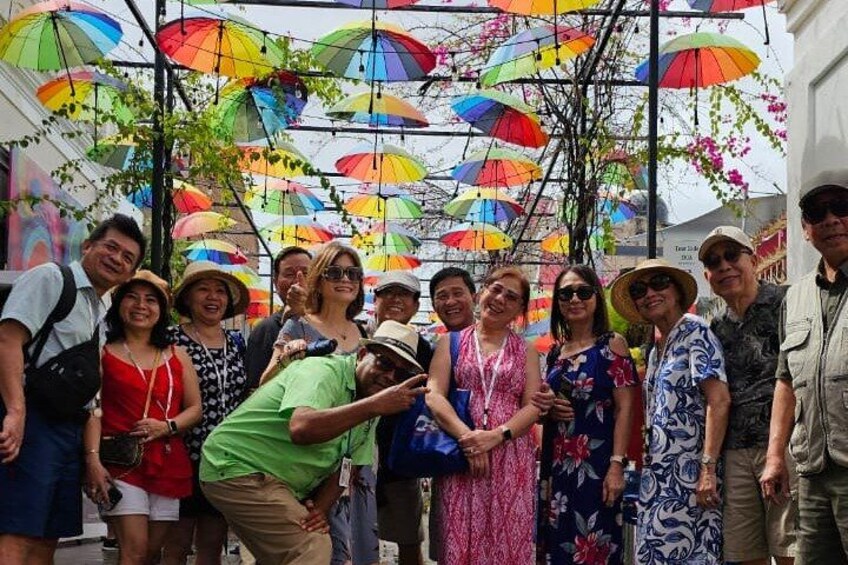 A group of people posing under a canopy of colorful umbrellas. 3
