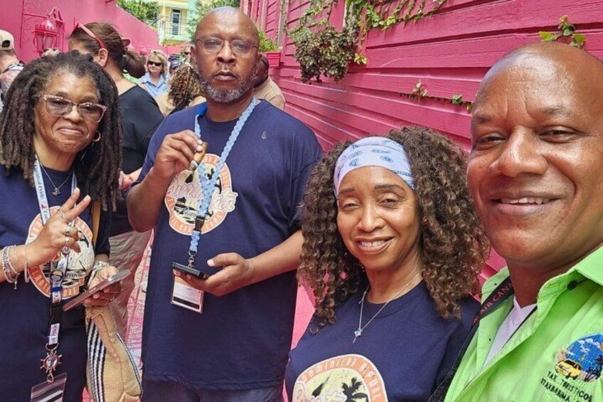 A group of people wearing matching t-shirts with a logo, standing in front of a pink building. 2
